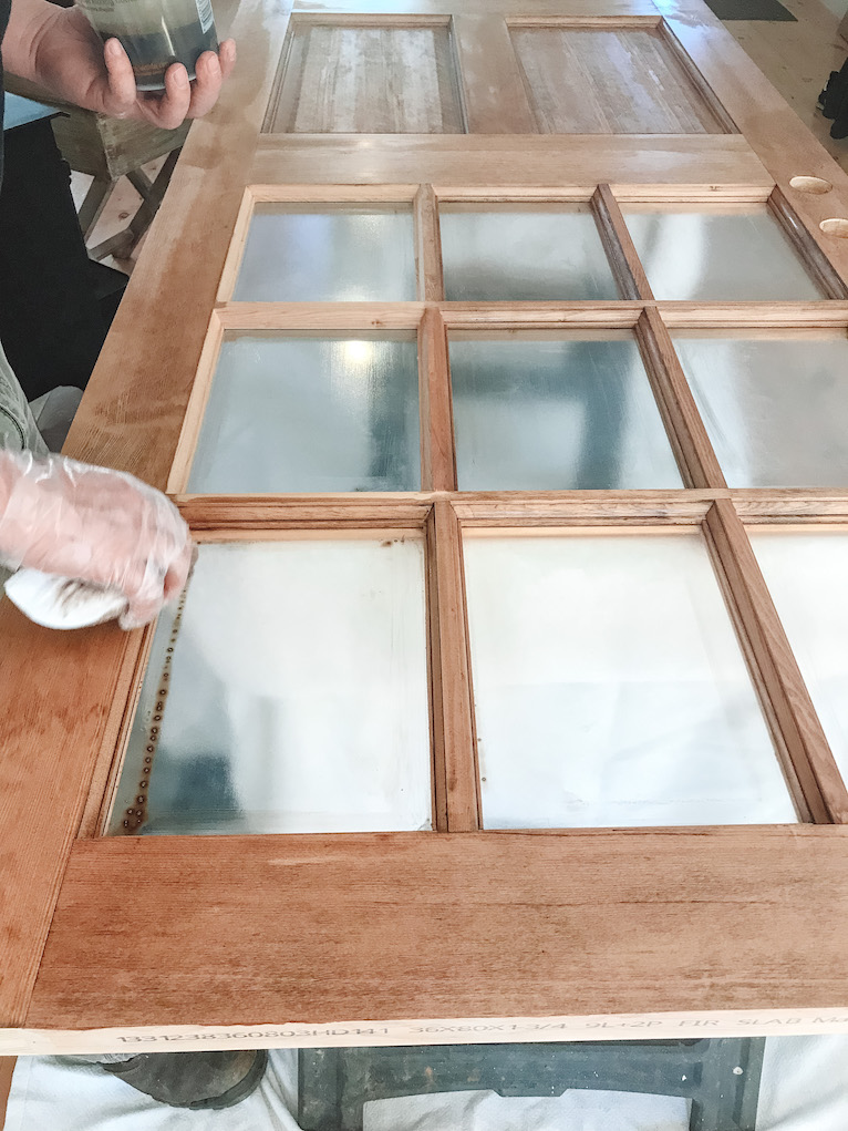 hand applying stain to wood door using a staining pad